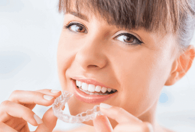How to get the most out of your invisalign treatment 6 Woman smiling while holding invisalign aligners, representing invisalign treatment, invisalign: fact vs. Fiction