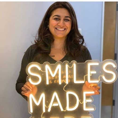 New patients 6 Dr. Parikh holding a neon sign that says smiles made here
