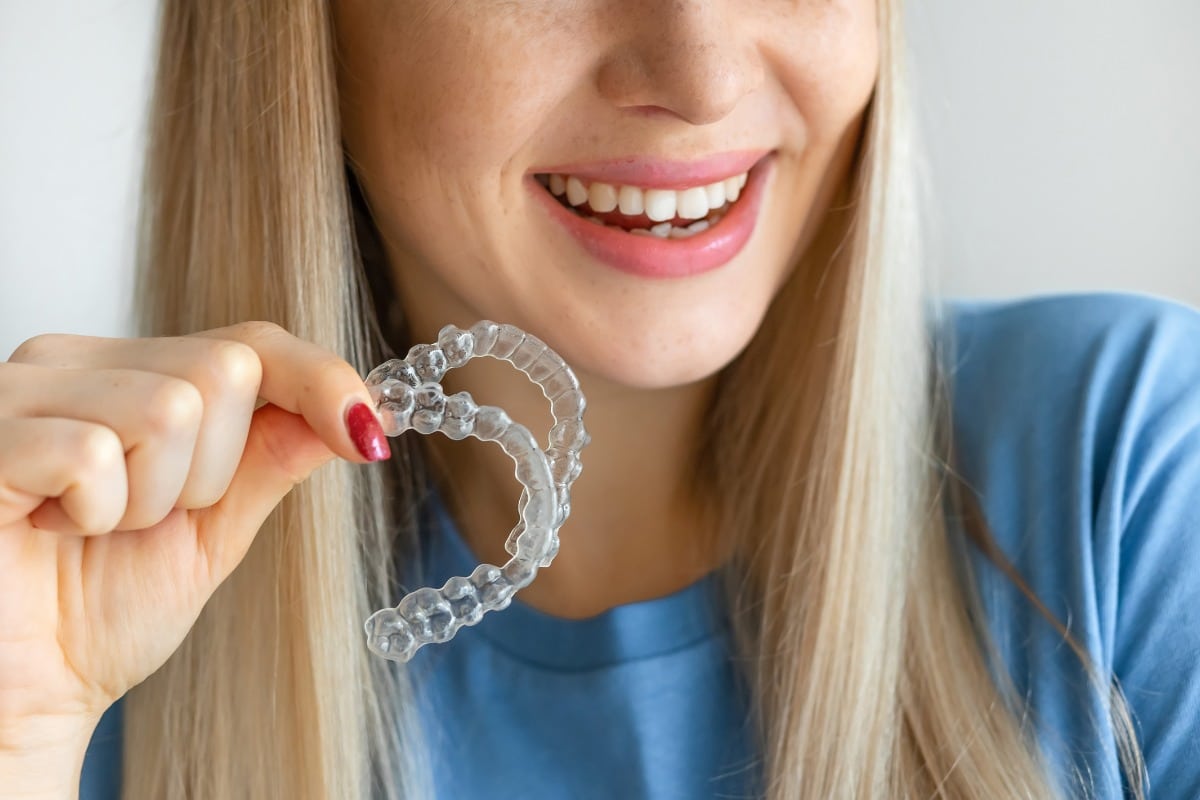 Smiling woman holding a clear essix retainer after orthodontic treatment.