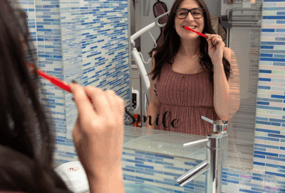How to care for braces properly—tips for comfort & care 7 Teenage girl smiling and brushing her teeth in front of a mirror, representing how to care for braces properly